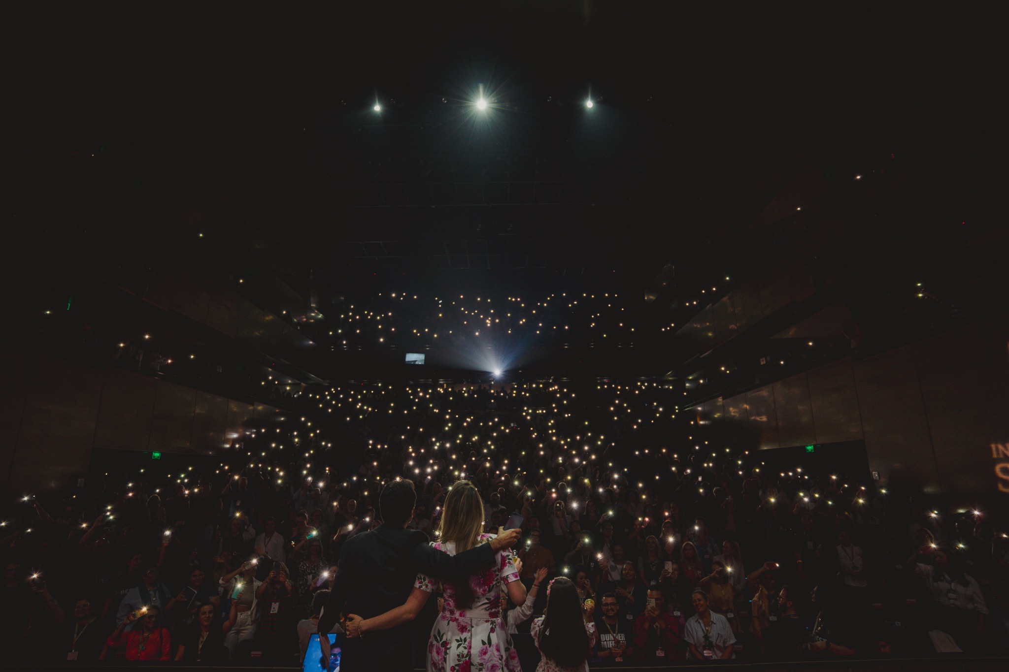 Plateia de evento corporativo iluminada pelos celulares do público
